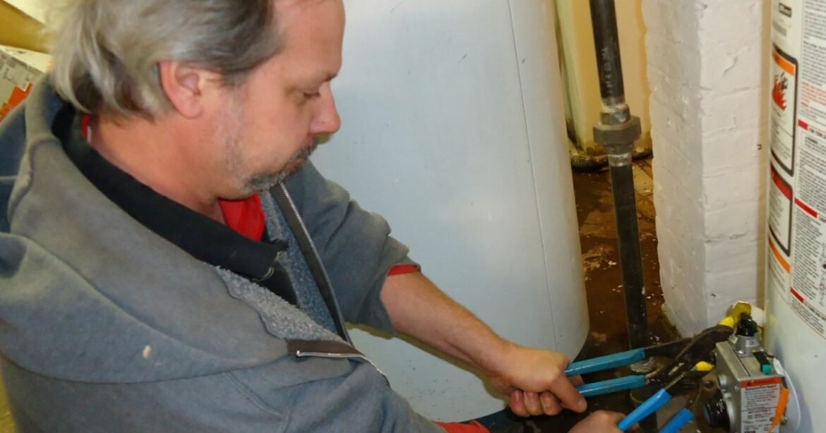 A plumber using two wrenches to tighten a pipe fitting, illustrating a professional home repair job