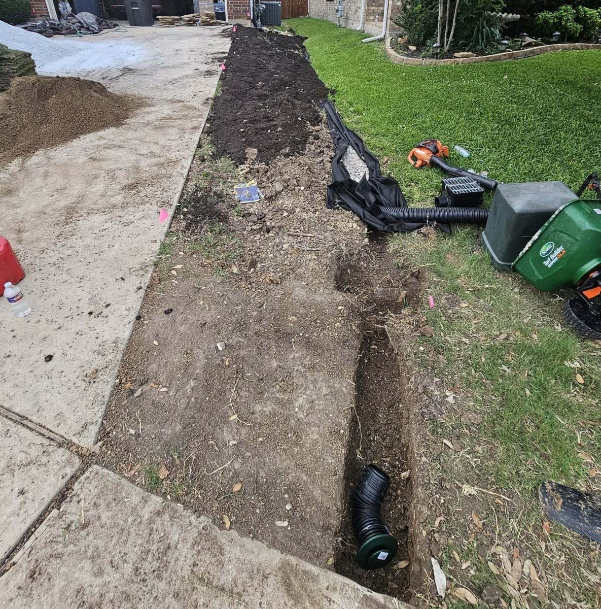 French drain trench with gravel and perforated pipe beside a Texas home foundation
