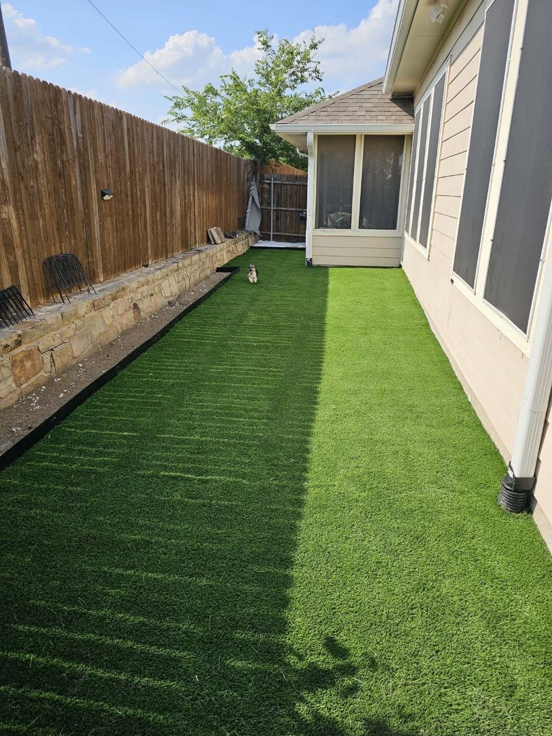 Finished artificial turf lawn in a narrow Texas back yard beside a stone retaining wall