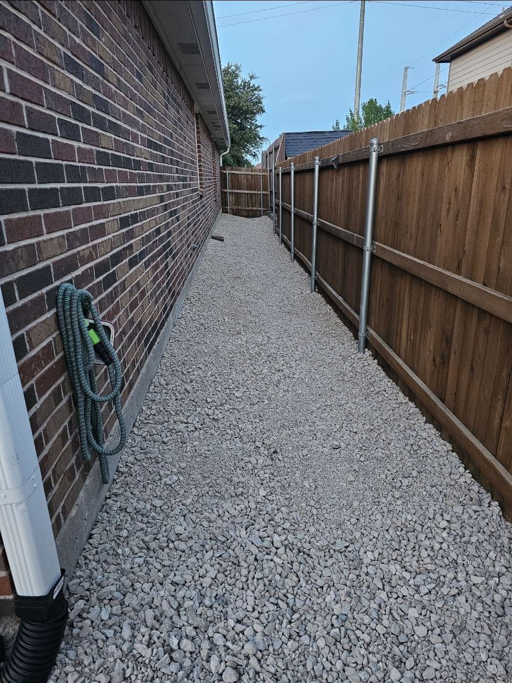 Finished gravel side yard over a French drain between a brick wall and a fence