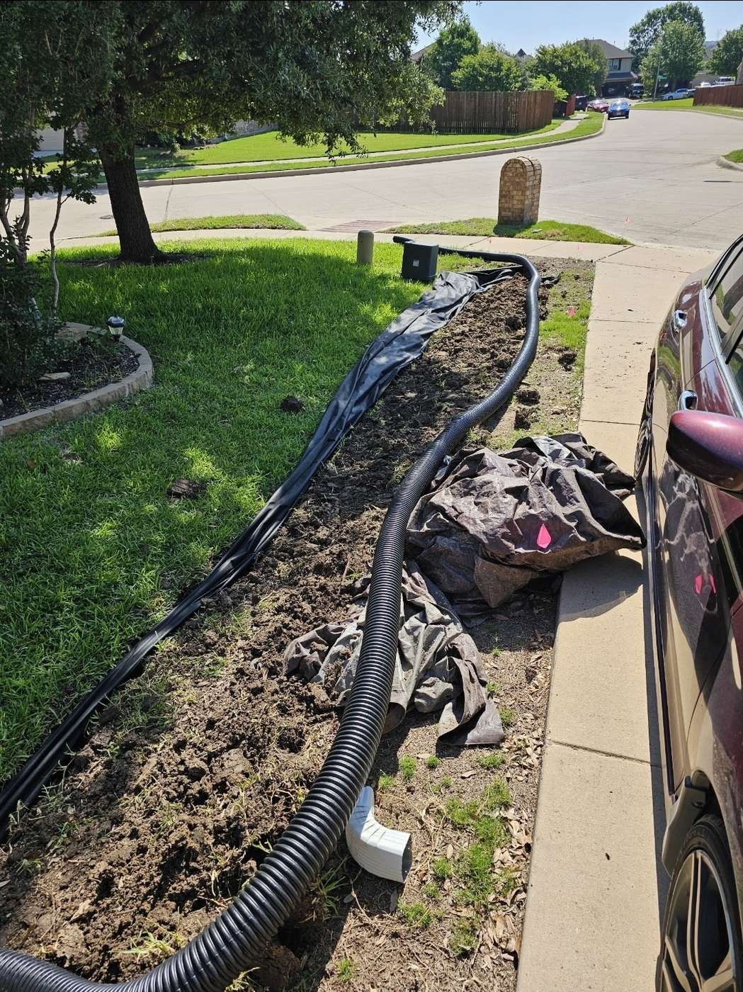 Corrugated French drain pipe running across a front lawn to discharge at the street curb