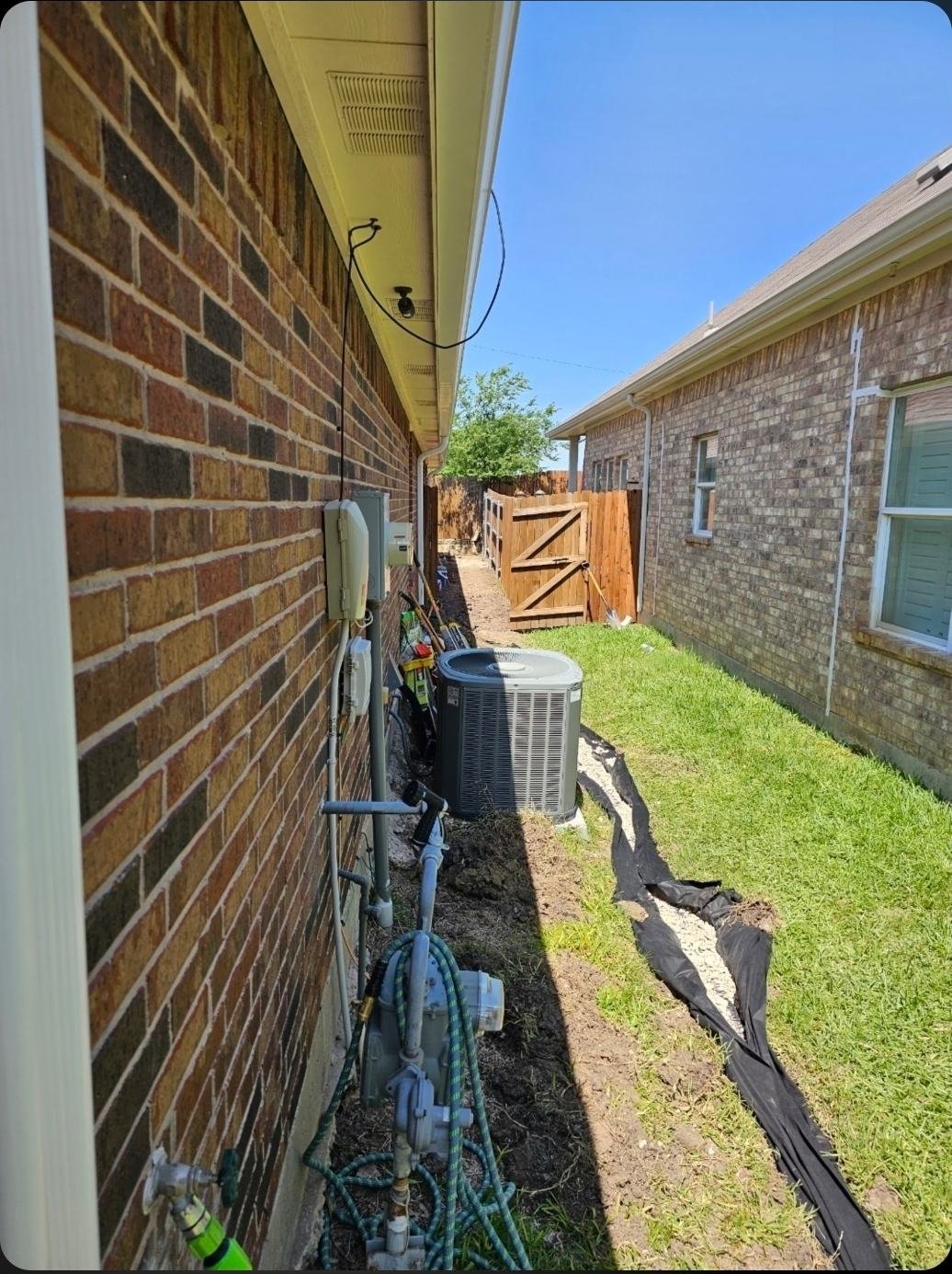 Open French drain trench lined with filter fabric routed past an air conditioner condenser