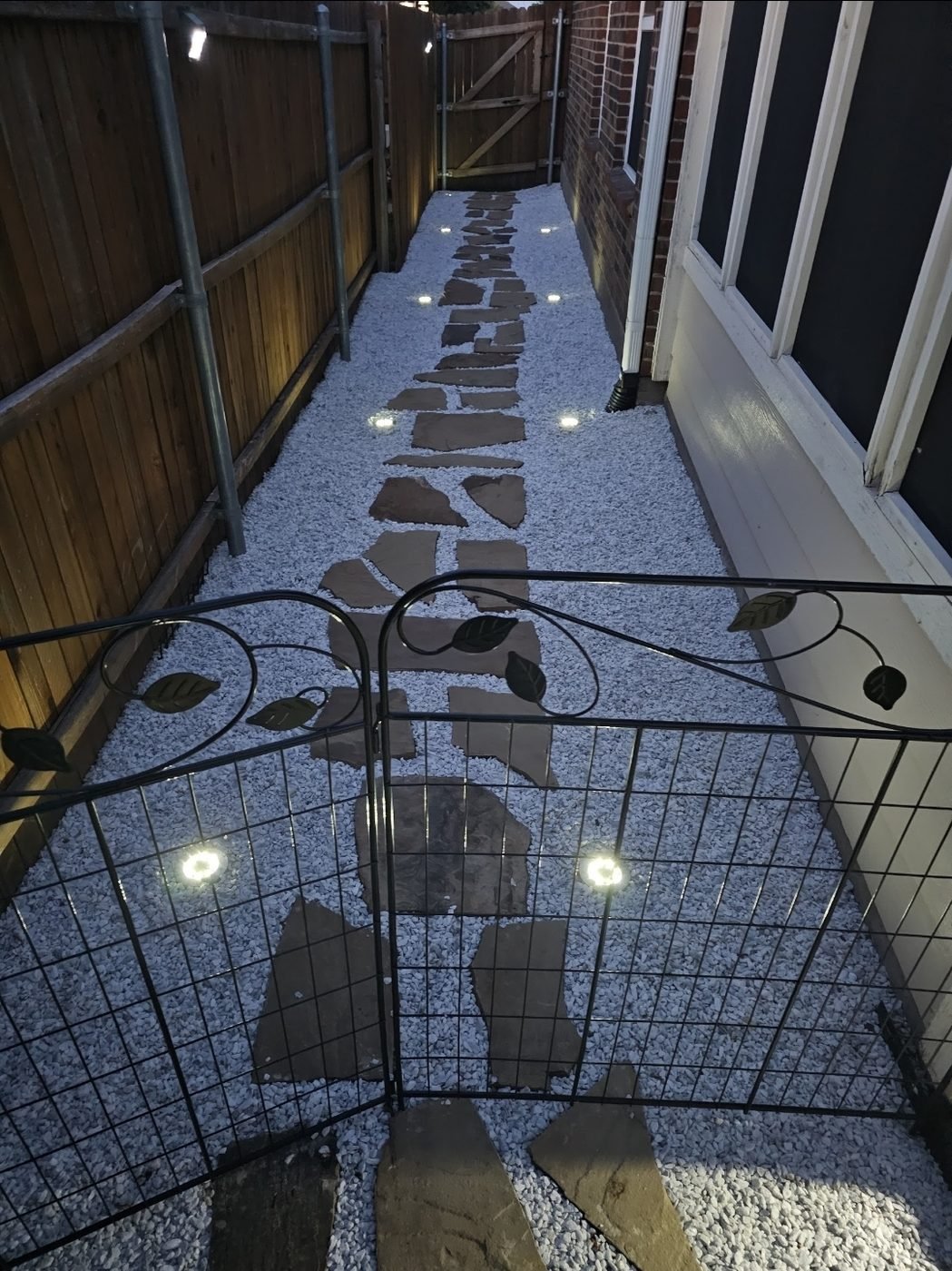 Finished gravel side yard with a flagstone path and low path lights at dusk, over a French drain